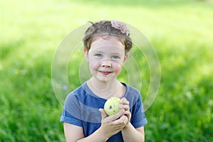 Adorable little preschool kid girl eating green apple on organic farm