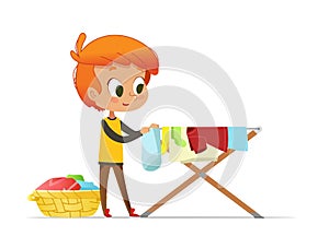 Adorable little redhead boy hanging washed clothes on drying rack isolated on white background. Home activity for kids