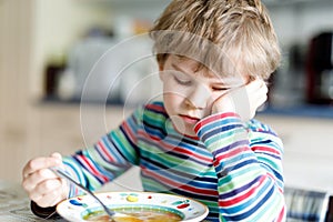 Adorable little school boy eating vegetable soup indoor.