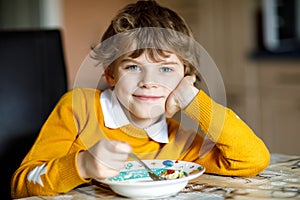 Adorable little school boy eating vegetable soup indoor.