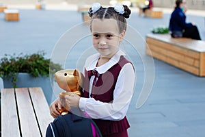 Adorable little school girl wearing stylish uniform holding her favorite toy golden mouse outdoors