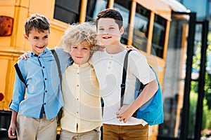 adorable little schoolboys embracing in front of school bus and looking photo