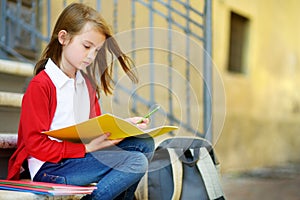 Adorable little schoolgirl studying outdoors on bright autumn day. Young student doing her homework. Education for small kids.