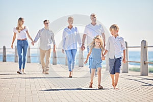 Adorable little sibling brother and sister holding hands while walking ahead on a seaside promenade while their parents