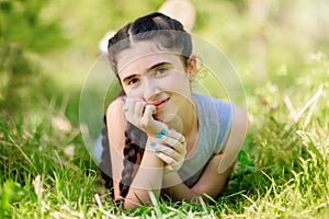 Adorable little smiling girl lying on grass in garden and keeping her hand under chin