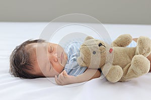 Adorable little sweet newborn baby girl sleeping on white bed with teddy bear doll, cute infant has good dream in bedroom