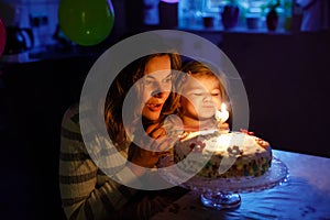 Adorable little toddler girl celebrating second birthday. Baby child daughter and young mother blowing candles on cake