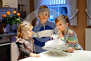 Adorable little toddler girl celebrating third birthday. Baby sister child and two kids boys brothers blowing together