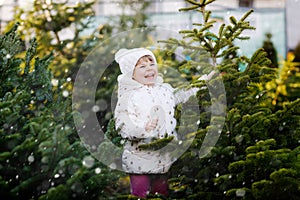 Adorable little toddler girl holding Christmas tree on market. Happy healthy baby child in winter fashion clothes