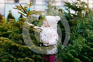 Adorable little toddler girl holding Christmas tree on market. Happy healthy baby child in winter fashion clothes