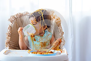 Adorable little toddler girl or infant baby drink water after eat delicious spaghetti food on chair. Funny cute infant girl get