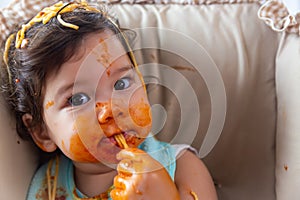 Adorable little toddler girl or infant baby eating delicious spaghetti food with tomato sauce. Funny cute infant girl get hungry