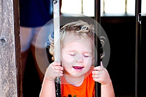 Adorable little toddler girl in pumpkin shirt behind bars.