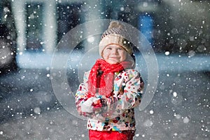 Adorable little toddler girl walking outdoors in winter. Cute toddler during strong snowfall on evening. Child having