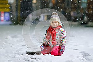 Adorable little toddler girl walking outdoors in winter. Cute toddler during strong snowfall on evening. Child having