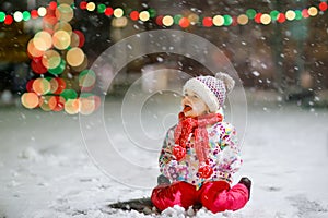Adorable little toddler girl walking outdoors in winter. Cute toddler during strong snowfall on evening. Child having