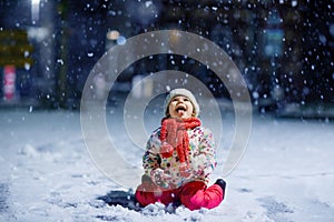 Adorable little toddler girl walking outdoors in winter. Cute toddler during strong snowfall on evening. Child having