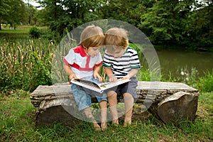 Adorable Little Twin Brothers Sitting on a Wooden Bench and Reading a Book Very Carefully Near the Beautiful Lake