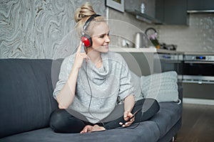 Adorable middle aged blond woman sitting on sofa in her home and listen to the music