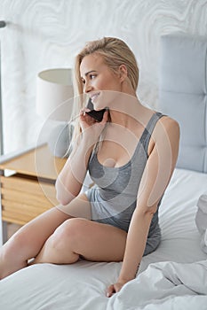 Adorable middle aged blonde woman sitting on bed and talking on mobile phone