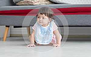 Adorable mixed race, Caucasian and Asian, little toddler baby girl wear apron, pink dress is smiling and crawling on floor at home