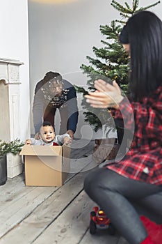 Adorable mixed-race toddler having fun while sitting in a carton box and being pushed by his father.Vertical Shot.