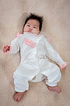 Adorable 3 month old newborn baby girl laying on the soft carpet and looking at the camera. The girl just woke up from her sleep