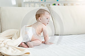 Adorable 10 months old baby boy in diapers sitting on sofa