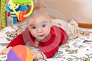 Adorable 6 months old little baby boy during tummy time surrounded by colourful toys