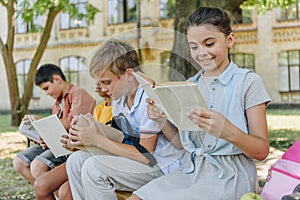 Adorable multicultural friends sitting on bench in schoolyard and reading books