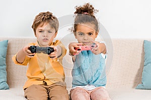 Adorable multiethnic kids playing video game with joysticks and looking