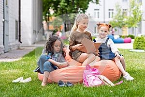 adorable multiethnic schoolgirls sitting on bean bag chair and reading book