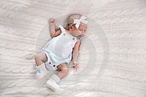 Adorable newborn baby with pacifier sleeping on white knitted plaid, top view. Space for text