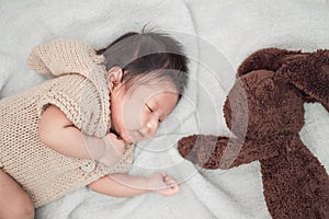 Adorable newborn baby peacefully sleeping with brown rabbit doll on a white blanket.