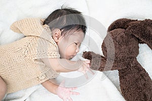 Adorable newborn baby peacefully sleeping with brown rabbit doll on a white blanket.