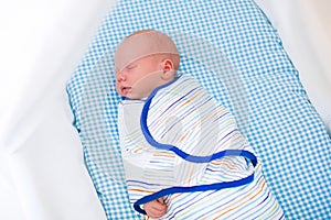 Adorable newborn baby sleeping swaddled in white bed.