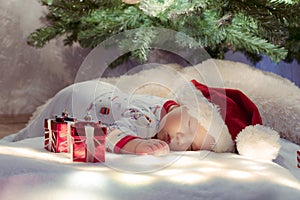 Adorable newborn baby sleeping under Christmas tree near gifts on lighting blanket