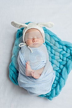 Adorable newborn child wearing bunny ears hat sleeping on a bed