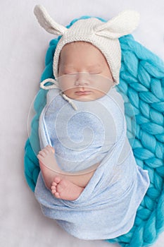 Adorable newborn child wearing bunny ears hat sleeping on a bed