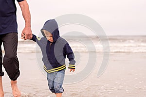 Adorable obedient toddler boy walking on a beach