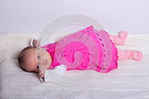 Adorable one month old baby girl in pink dress lies on a soft blanket