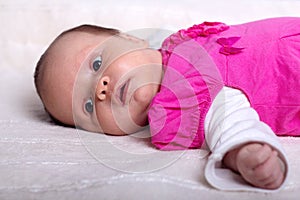 Adorable one month old baby girl in pink dress lies on a soft blanket