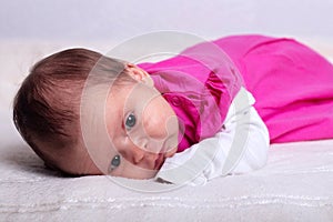 Adorable one month old baby girl in pink dress lies on a soft blanket