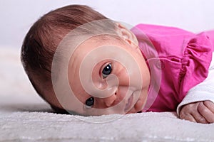 Adorable one month old baby girl in pink dress lies on a soft blanket