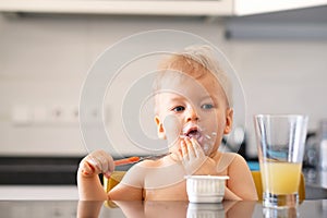 Adorable one year old baby boy eating yoghurt with spoon