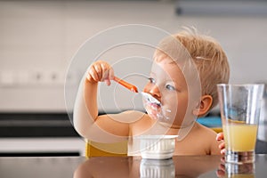 Adorable one year old baby boy eating yoghurt with spoon