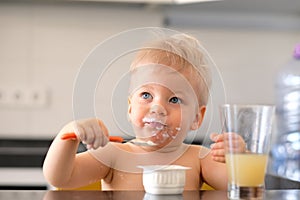 Adorable one year old baby boy eating yoghurt with spoon