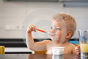 Adorable one year old baby boy eating yoghurt with spoon