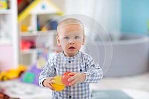 Adorable one year old baby in playroom. Child boy playing with colorful toys at home. Early development, learning and