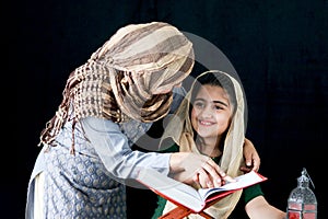 Adorable Pakistani girl with beautiful eyes wear hijab, learning Quran book with mother, Muslim family, daughter and mom read holy